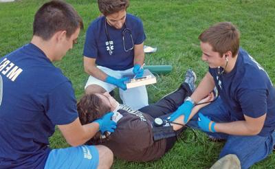 Three Medical Emergency Response Team members assist a fallen student in a training drill